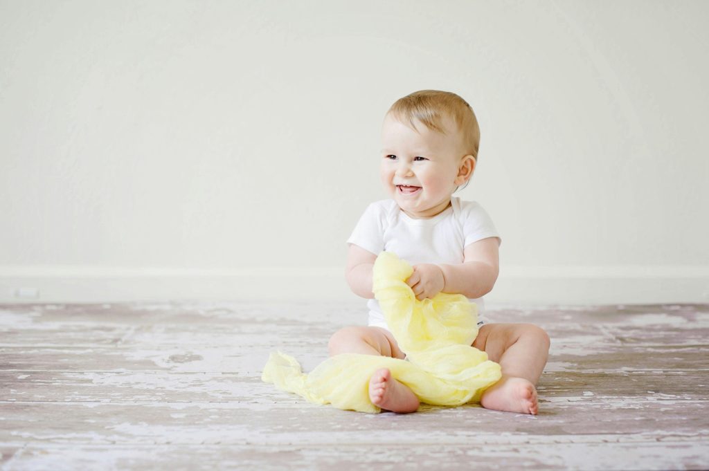 Adorable baby laughing while sitting on the floor with a yellow blanket indoors, showcasing happiness and innocence.